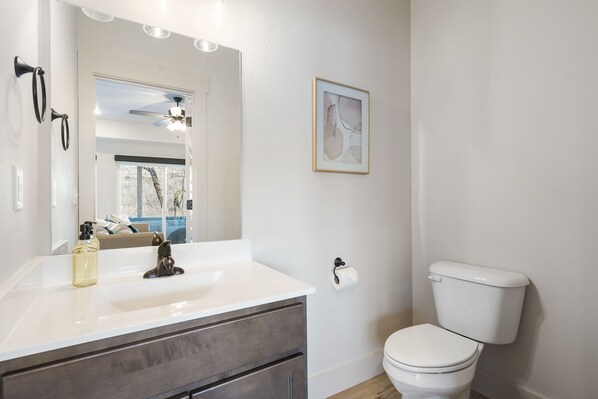 A bathroom with a white sink, dark cabinet, toilet, and a framed abstract art piece on the wall.