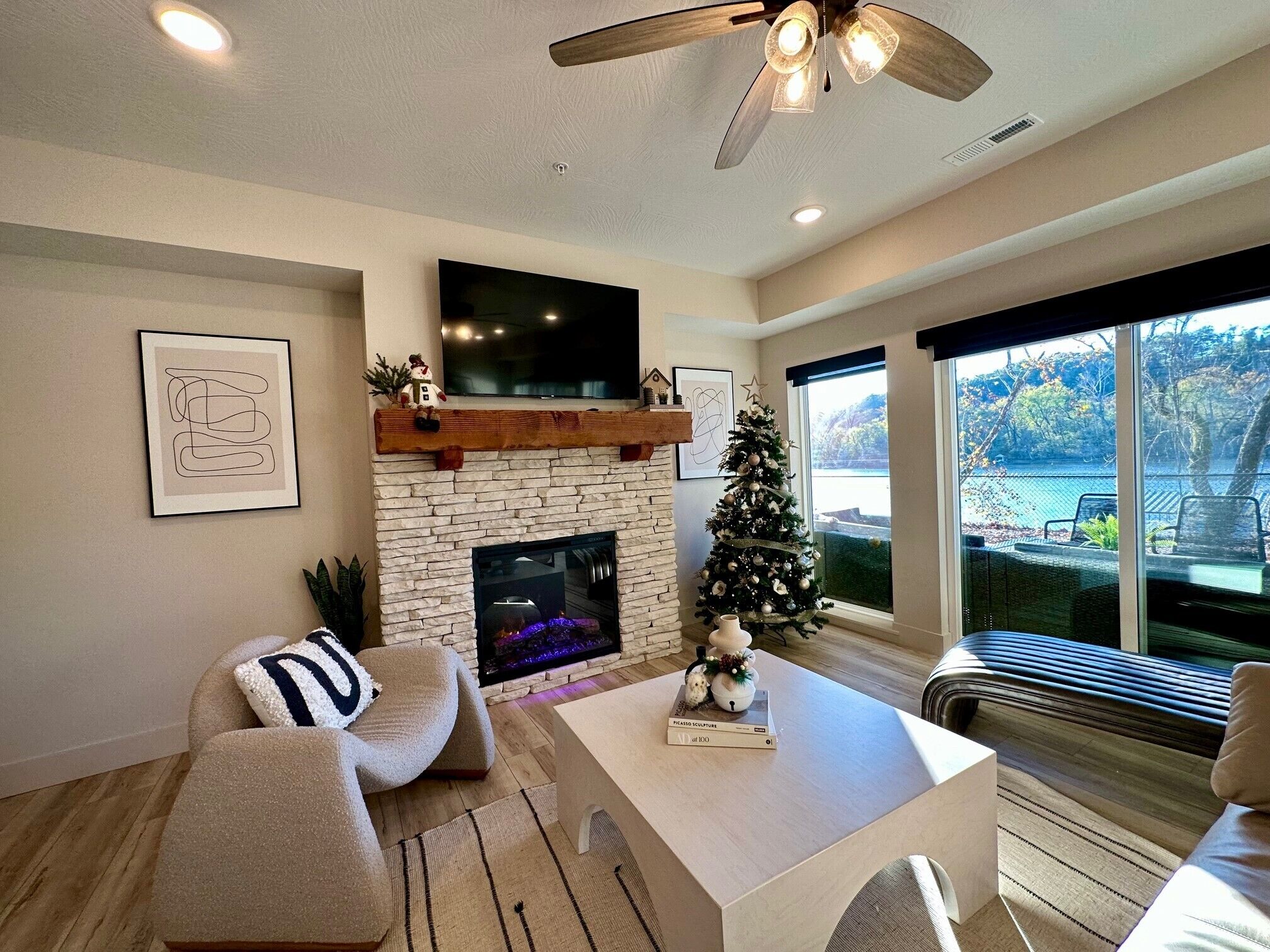 A modern living room with a stone fireplace, a flat-screen TV mounted above it, and a Christmas tree.