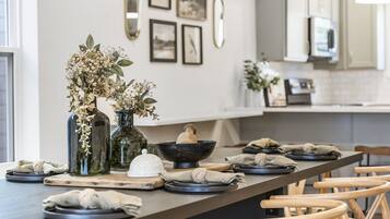 Una cocina moderna con una isla grande, sillas de madera y una mesa de comedor dispuesta con platos, tazones y un florero con flores secas.