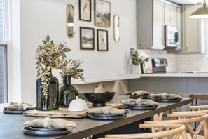 Une cuisine moderne avec un grand îlot central, des chaises en bois et une table à manger dressée avec des assiettes, des bols et un vase contenant des fleurs séchées.