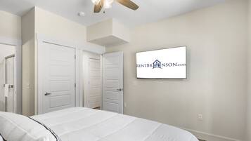 Un dormitorio con cama, dos puertas, un ventilador de techo y un televisor montado que muestra un logotipo.