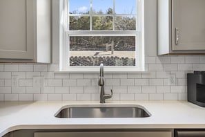 A kitchen with a stainless steel sink, white tiled backsplash, and a window overlooking a garden. - Private Hot Tub Retreat with Stunning Lake Views, Games & Near Branson Landing (Branson)