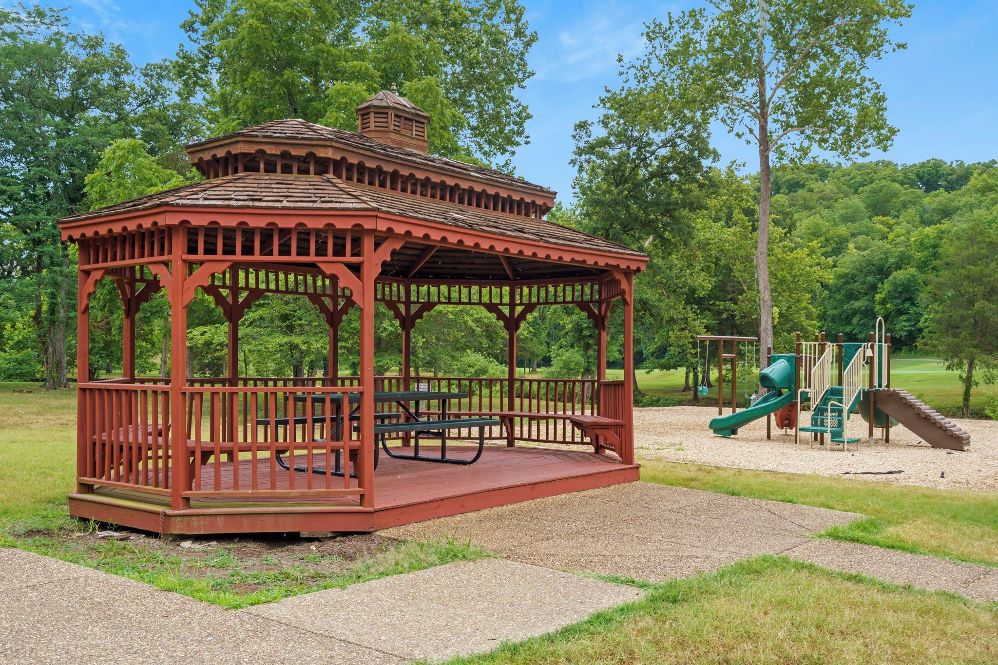 A gazebo with a picnic table and benches, surrounded by a playground with slides and swings.