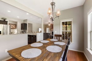 A dining room with a long wooden table, four placemats, and a chandelier. - Renovated Cabin with Screened-In Porch, Life-Size Games, Community Pools & Free Tickets Near SDC (Reeds Spring)