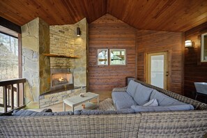 A cozy cabin interior with a stone fireplace, wooden walls, a wicker sofa, and a small table.