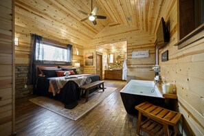 A wooden cabin interior with a bed, bench, and a bathroom with a bathtub.