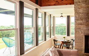 A sunlit room with large windows, a fireplace, and a dining area with chairs and a table.