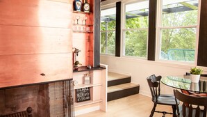 Een gezellig interieur met een houten wand, een glazen tafel met stoelen, en een raam met uitzicht op groen.