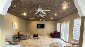 Un salon spacieux avec un plafond haut, un ventilateur de plafond, un téléviseur à écran plat et une cheminée.