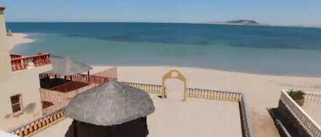 Une vue sur la plage avec une structure à toit de chaume, une plage de sable et un bâtiment doté de balcons.