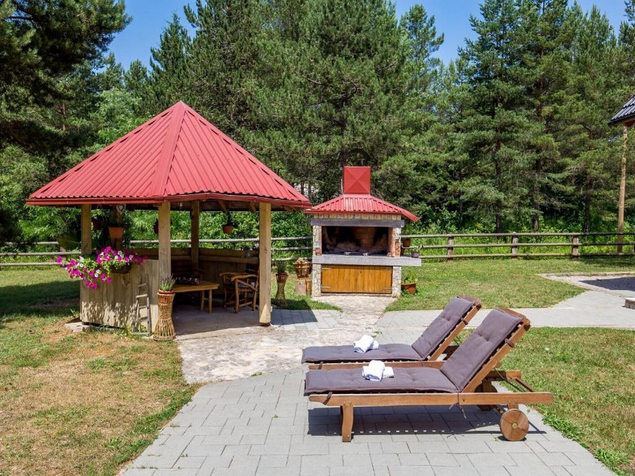 En lusthus med ett rött tak, en grillplats och solstolar.