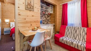A cozy cabin interior with a dining area, a kitchenette, and a living space with a red sofa and patterned throw. - Apartments Plitvice forest - One Bedroom Apartment with Terrace (Plitvicka Jezera)