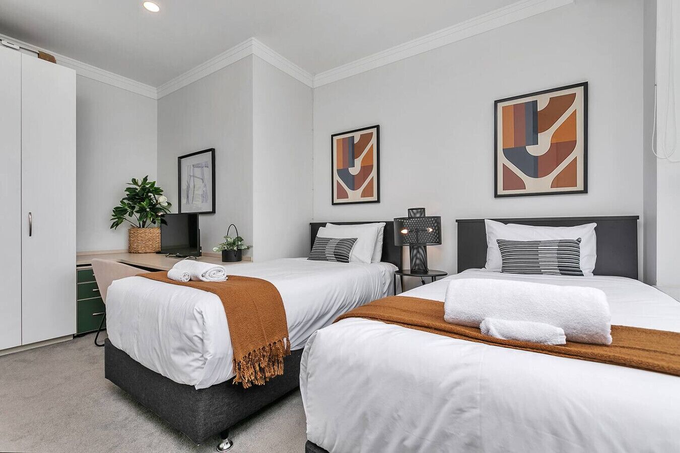 Een hotelkamer met twee bedden, een bureau, een stoel, een plant en kunstwerken aan de muren.