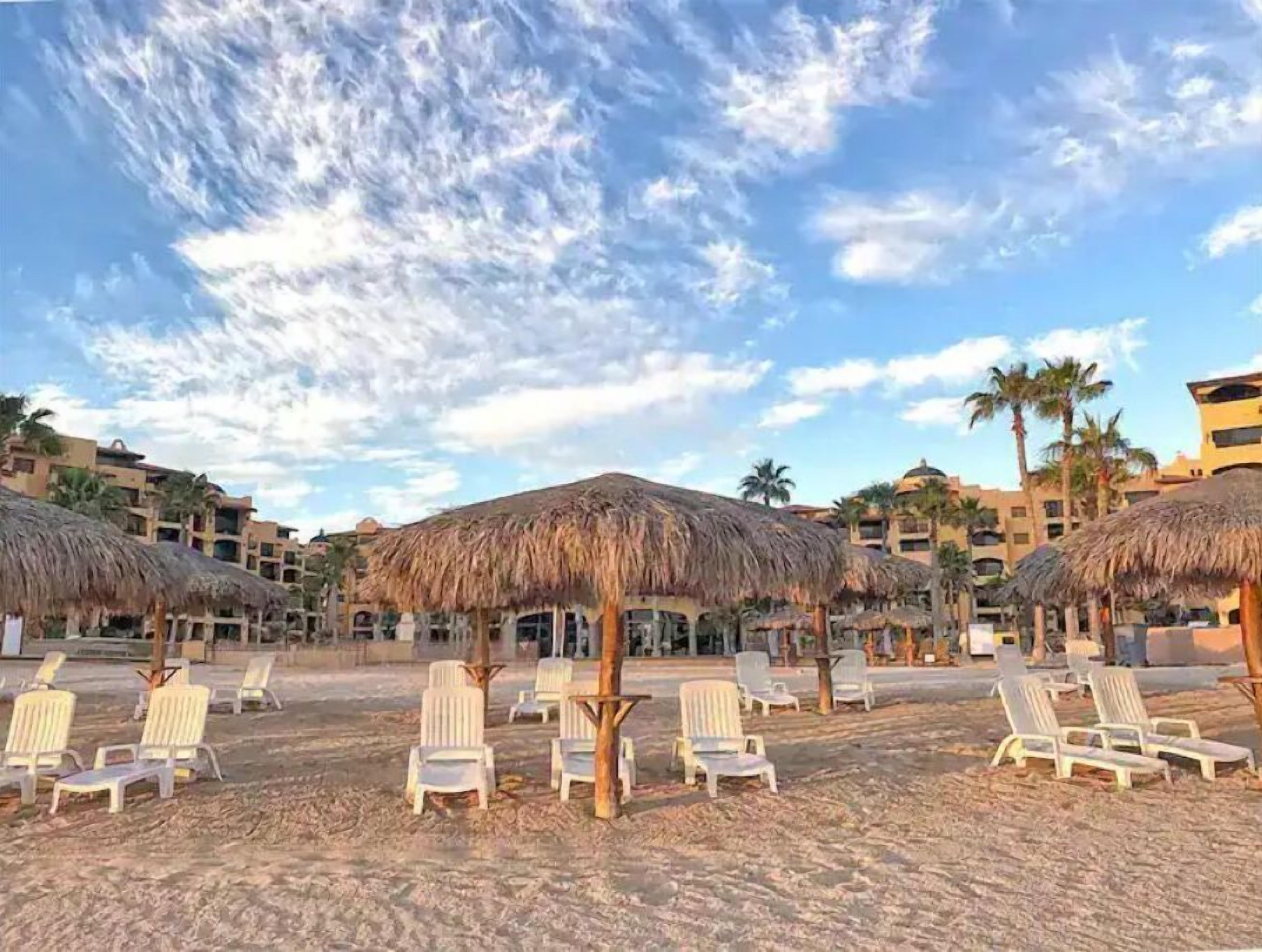 A beach resort with thatched umbrellas and white lounge chairs.