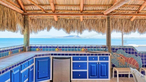 A covered outdoor area with a thatched roof, blue cabinets, and a view of the ocean. - Vacation Getaway Steps from the Water! (Choya Bay)
