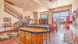 A spacious kitchen with a central island, a staircase with decorative railings, and a large window providing a view of the outside. - Vacation Getaway Steps from the Water! (Choya Bay)