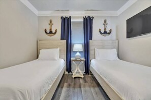 Two single beds with white linens, a flat-screen TV, and a small table in a clean and minimalistic room.