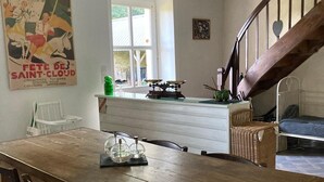 A rustic dining area with a wooden table and chairs, a kitchen counter with a green bottle, and a staircase with a wooden railing. - Beautiful Traditional Breton House in the Forest (Meslan)