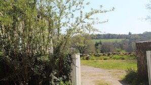 A rural pathway leading to a gate, surrounded by dense vegetation and a distant view of fields and trees. - Beautiful Traditional Breton House in the Forest (Meslan)