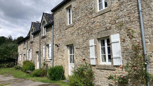 A stone building with multiple windows and shutters, a gravel path, and some greenery. - Beautiful Traditional Breton House in the Forest (Meslan)