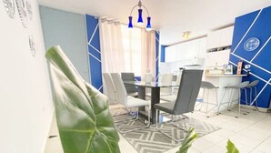 A modern dining area with a glass table and chairs, a blue accent wall, and a kitchen in the background. - Casa PIÑA, 3 bedroom condo & gated area (Fajardo)