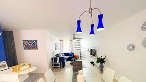 A modern living room with a glass dining table, white chairs, a blue sofa, and a staircase leading to an upper level. - Casa PIÑA, 3 bedroom condo & gated area (Fajardo)