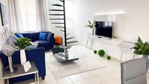 A modern living room with a blue sofa, a glass coffee table, a TV, and a spiral staircase. - Casa PIÑA, 3 bedroom condo & gated area (Fajardo)