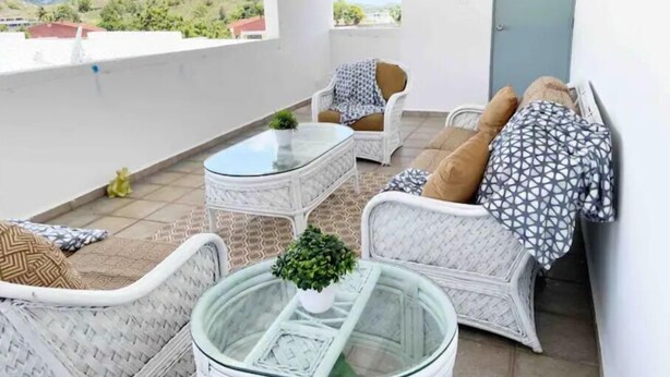 A balcony with wicker furniture, a glass coffee table, and a view of greenery. - Casa PIÑA, 3 bedroom condo & gated area (Fajardo)