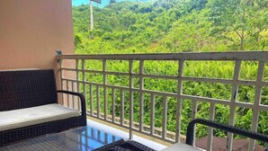 A balcony with wicker furniture and a glass table, overlooking a lush green landscape. - Lovely 3 bedroom condo with pools & gated area. (Fajardo)
