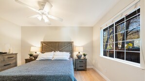 Ein Schlafzimmer mit Bett, Nachttischen, Deckenventilator und einem großen Fenster.