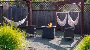 Eine Terrasse mit Feuerstelle, zwei Korbstühlen, einer Hängematte und einer Holzpergola.