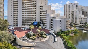 A multi-story hotel with a central courtyard, parking area, and a body of water. - Oceanfront 11th-Floor End Unit | Quiet & Private | Walk to Barefoot Landing (Myrtle Beach)