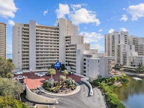 A multi-story hotel with a central courtyard, parking area, and a body of water.