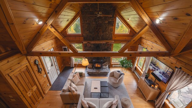 L’intérieur d’un chalet confortable, avec une cheminée en pierre, des poutres en bois, un canapé et une table basse.