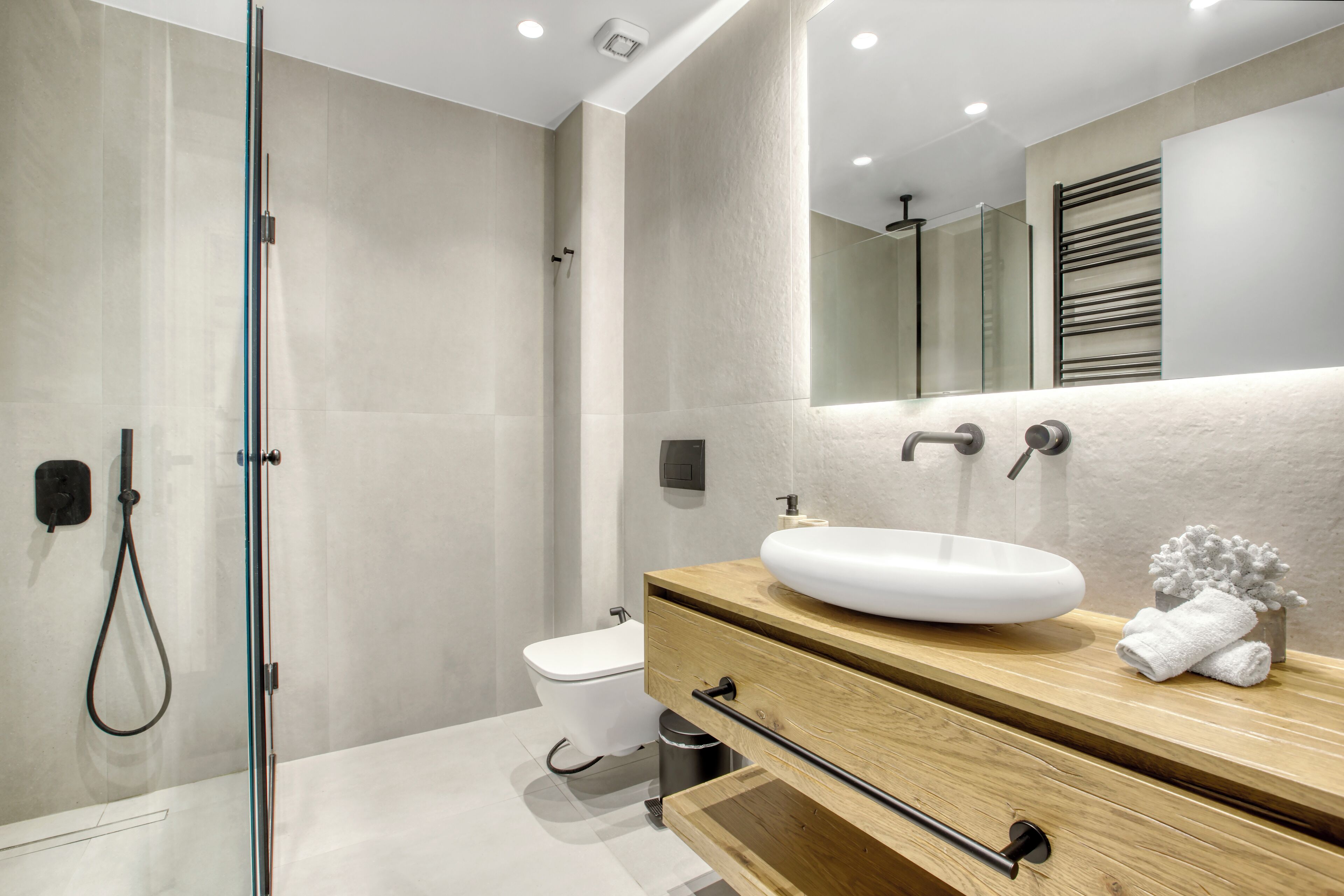 A modern bathroom with a glass shower enclosure, a white sink, and a wooden vanity.