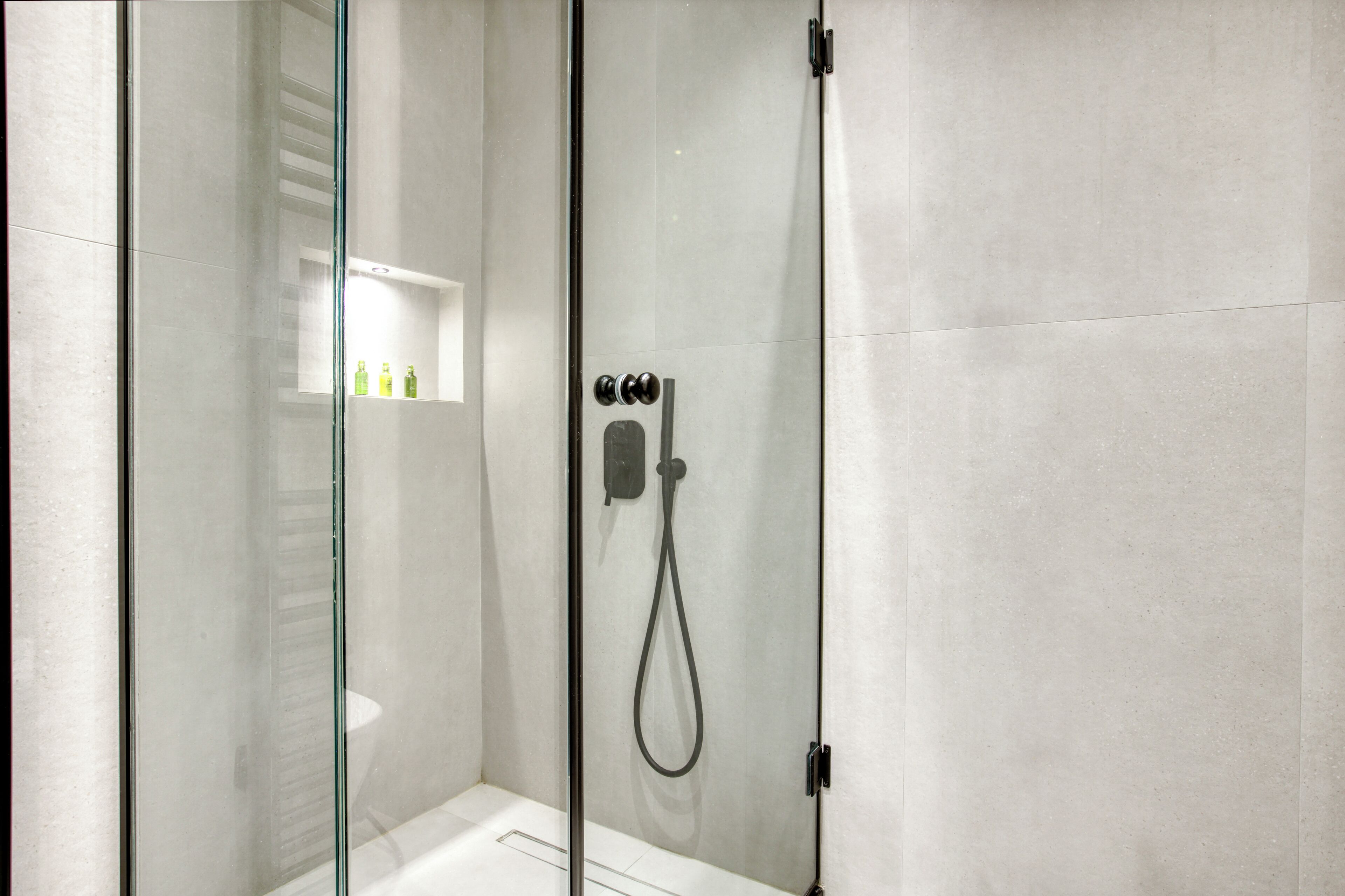 A modern shower area with a glass door, a handheld showerhead, and a control panel.
