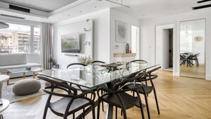 A modern living room with a glass dining table, dark chairs, a white sofa, and a large window offering a city view. - Kallirrois 89 Suite (Athens)