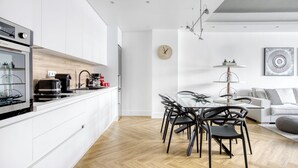A modern kitchen with white cabinets, a wooden countertop, and a dining area with a glass table and black chairs. - Kallirrois 89 Suite (Athens)