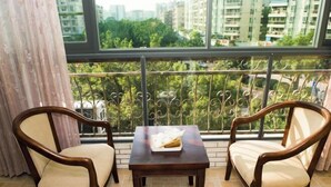 A balcony with two wooden chairs and a small table, a view of a cityscape through a large window, and a curtain partially covering the window. - Jinxin Yixiang Hotel (Meizhou)