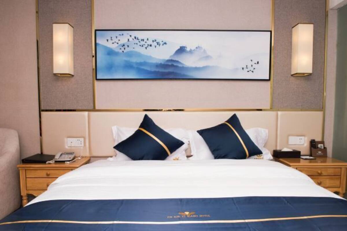 A hotel room with a large bed, two bedside tables, a nightstand, and a wall-mounted artwork.