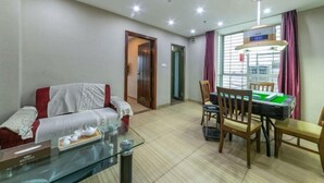 A living room with a sofa, a glass coffee table, and a dining table with chairs. - Jinxin Yixiang Hotel (Meizhou)