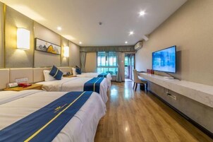 A hotel room with three beds, a desk, a TV, and a window with curtains.