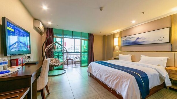 A hotel room with a bed, desk, chair, TV, and a view of the outdoors. - Jinxin Yixiang Hotel (Meizhou)