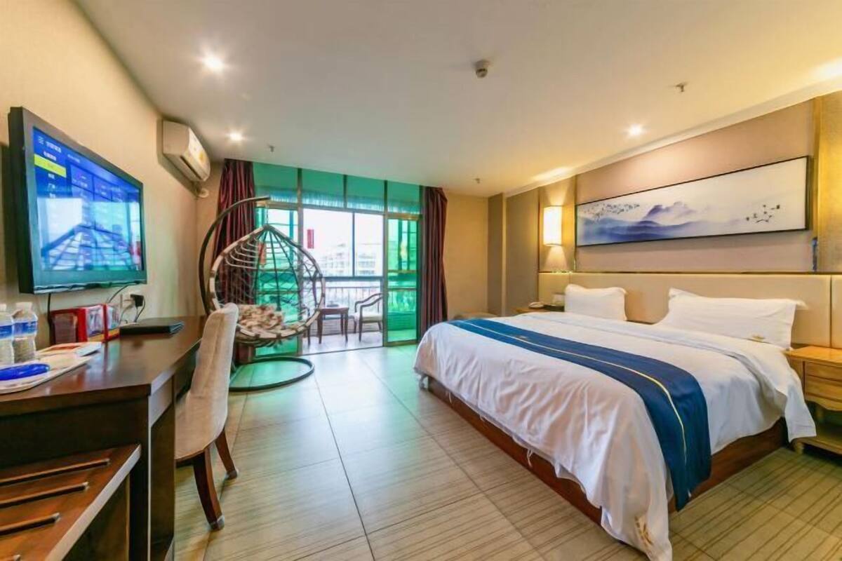 A hotel room with a bed, desk, chair, TV, and a view of the outdoors.