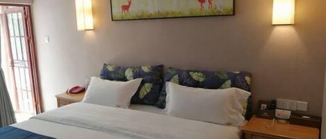 Una habitación de hotel con una cama, dos almohadas, una mesita de noche, una lámpara y un cuadro en la pared.