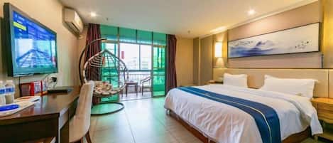 A hotel room with a bed, desk, chair, TV, and a view of greenery.