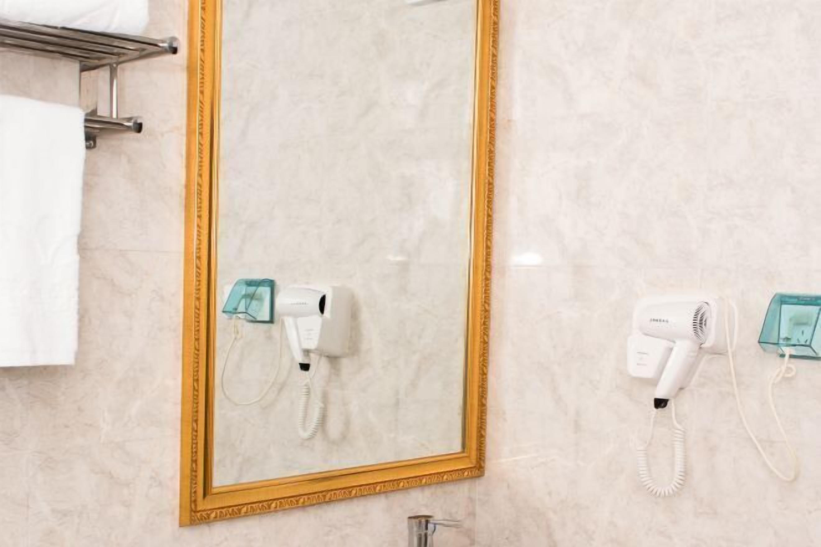 A bathroom with a marble wall, a gold-framed mirror, and two hair dryers mounted on the wall.