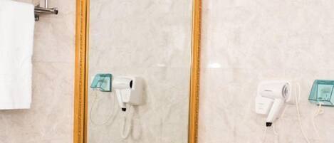 A bathroom with a marble wall, a gold-framed mirror, and two hair dryers mounted on the wall.