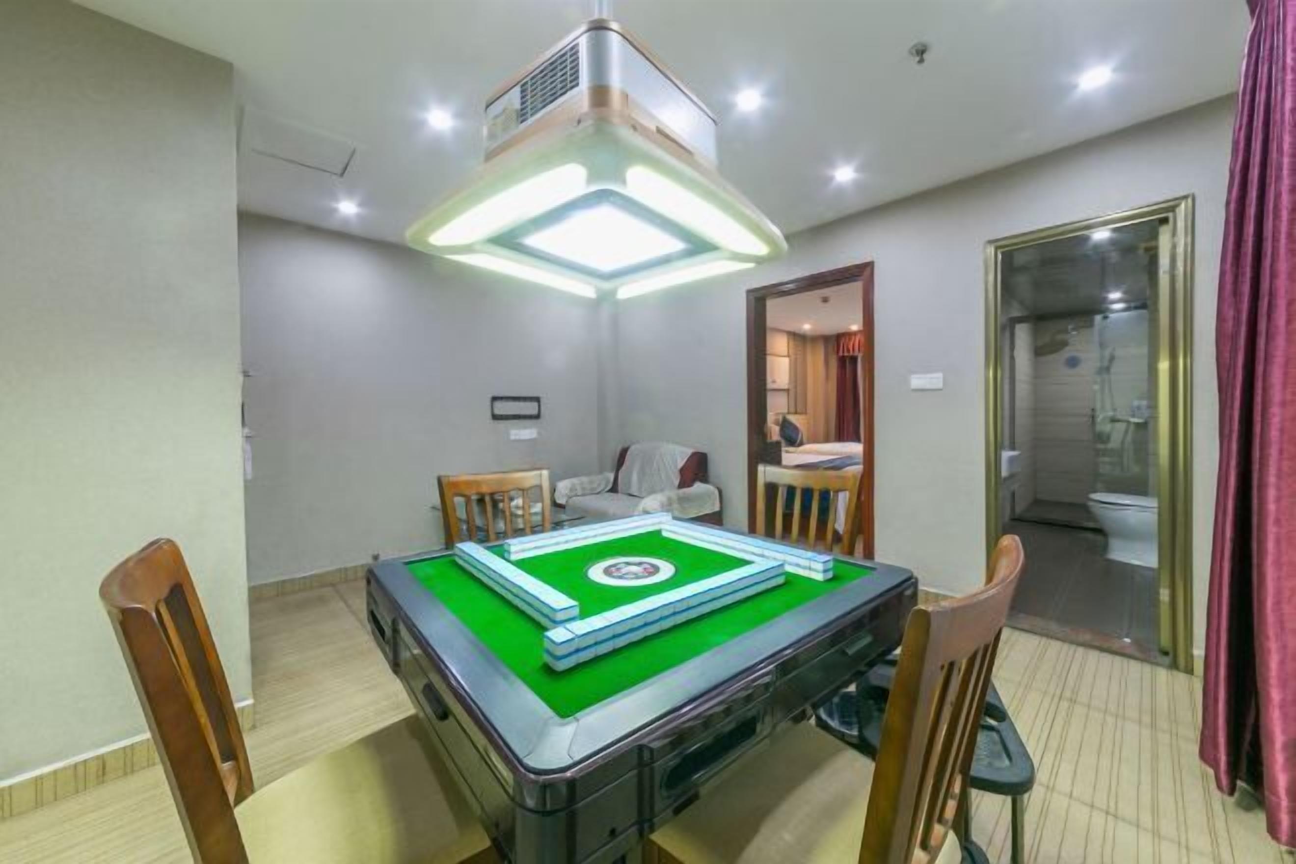 A room with a pool table, a ceiling-mounted air conditioner, a small seating area with a sofa and chairs, and a bathroom visible through a glass door.