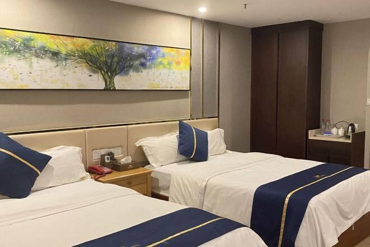 A hotel room with two beds, a nightstand, a wardrobe, and a painting on the wall.